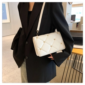 Detail of white quilted crossbody bag with golden studs and metal buckle on leather strap