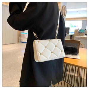 Detail of white quilted crossbody bag with golden rivets and adjustable shoulder strap