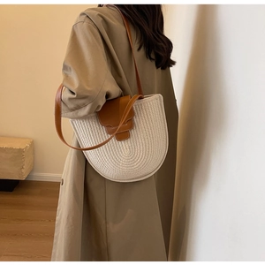 Close-up of woven bucket bag with brown leather strap on model in elegant studio setting