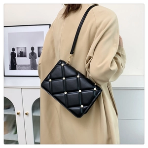Detail of black quilted shoulder bag with gold studs on a model in a modern home interior