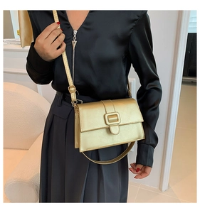 Close-up of champagne gold crossbody bag with metallic finish and square buckle on a model