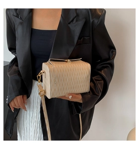 Détail du sac bandoulière plissé beige avec fermoir doré porté avec un blazer noir