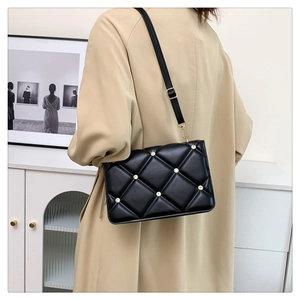 Detail of black quilted shoulder bag with rhinestones shown on model in a beige coat
