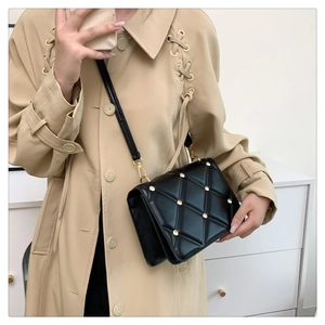 Detail of black quilted leather shoulder bag with gold studs and chain strap shown on model