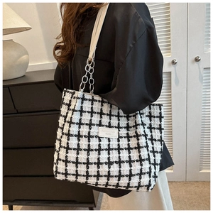 Detail shot of a black and white checkered tote bag with chain strap on a model shoulder