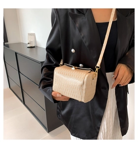 Détail de la texture plissée beige d'un sac cylindrique avec ferrures dorées