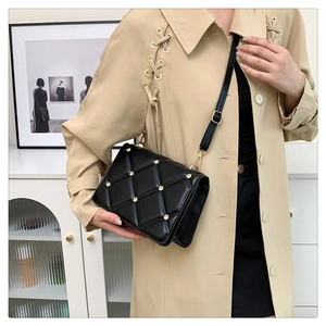 Detail of black quilted leather shoulder bag with gold rivets and adjustable strap