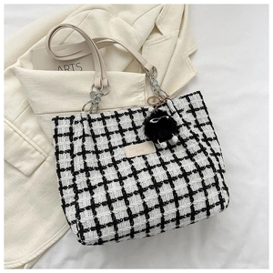 Macro detail of black and white checkered tweed tote bag with silver chain strap and pompom