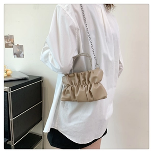 Detail of beige pleated cloud bag with rhinestone handle and silver chain strap