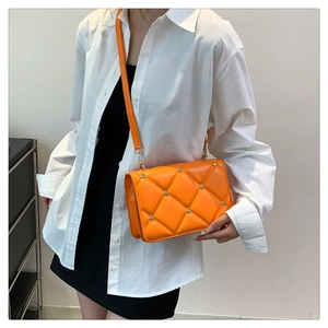 Close-up of bright orange quilted crossbody bag with metal stud details on model