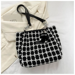 Detail of checkered tweed tote bag featuring black leather handles and cute eye charm