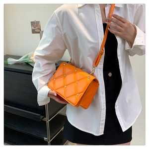 Detail of an orange quilted crossbody bag with silver studs worn by a model