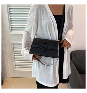Minimalist black patent leather square crossbody bag with magnetic flap closure worn by model