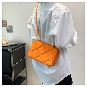 Model wearing bright orange quilted crossbody bag with metal rivets on minimalist interior