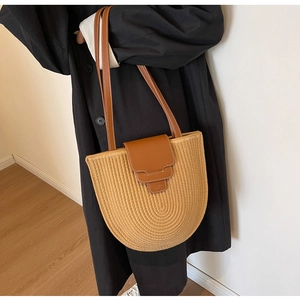 Detail of hand-woven beige bucket bag with dark brown leather strap and magnetic closure