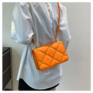 Side view of a bright orange quilted crossbody bag with metal rivets on a white shirt