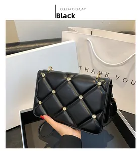 Detail of black quilted crossbody bag with stud accents next to white gift packaging