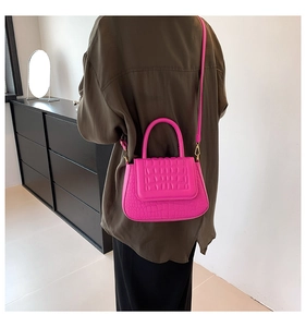 Detail van felle roze crossbodytas met krokodillenreliëf en gouden hardware op een model