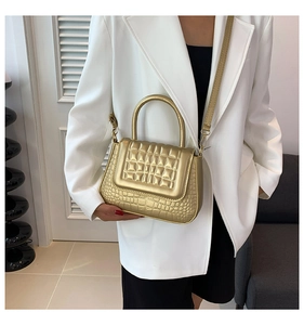 Detailopname van gouden tas met krokodillenmotief gedragen met witte blazer