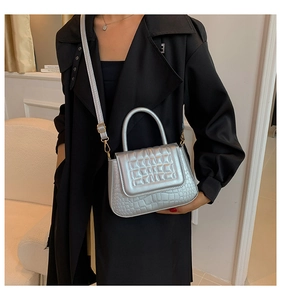 Zilveren tas met krokodillenpatroon als crossbody gedragen op een zwarte trenchcoat