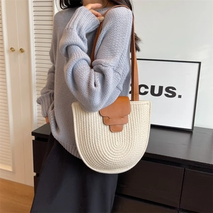 Minimalist cream woven straw shoulder bag with brown leather strap worn by a model