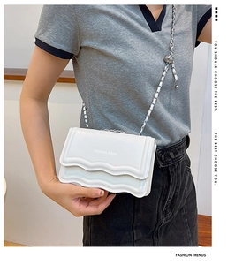 Detail of white wave-edge flap bag with metal chain strap and decorative silver ball