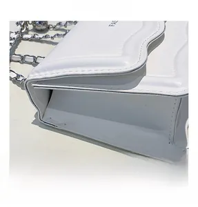 Close-up of white crossbody bag showing textured leather, wavy flap, and metal chain strap