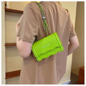 Détail du sac à bandoulière vert néon avec rabat festonné et texte argenté sur chaîne