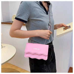 Détail du sac bandoulière rose avec bords festonnés et bandoulière chaîne sur un modèle