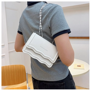 Gros plan d'un sac bandoulière blanc à bords ondulés avec chaîne porté par un modèle
