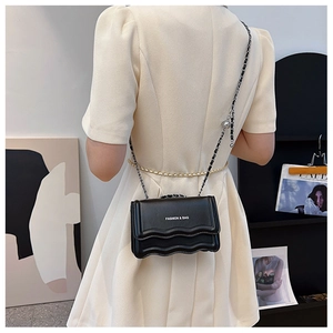 Détail d'un sac bandoulière noir avec rabat ondulé et bandoulière chaîne sur mannequin