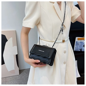Detail of black crossbody bag with gold chain strap and wavy flap edge on model