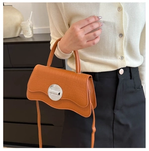 Detail of orange crocodile pattern handbag with unique wavy flap and silver metal buckle