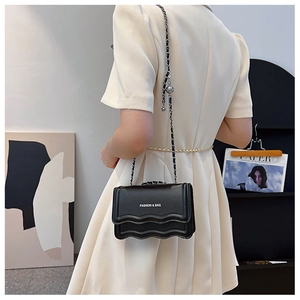 Détail du sac bandoulière noir avec bord ondulé et chaîne sur une robe blanche