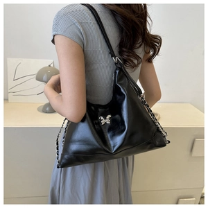 Detail of black glossy faux leather shoulder bag featuring silver metal butterfly logo