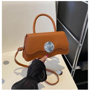 Detail of caramel crocodile pattern handbag with silver round metal buckle and top handle