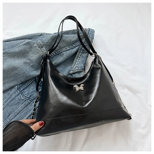 Detail of black PU leather tote bag with silver metal bow and stylish chain accents