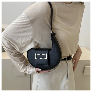 Détail du sac baguette noir en cuir croco avec boucle dorée porté par un mannequin