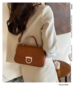 Detail of caramel brown handbag featuring gold D-buckle and adjustable shoulder strap