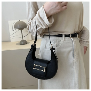 Détail d'un sac demi-lune noir motif crocodile avec boucle dorée porté à l'épaule