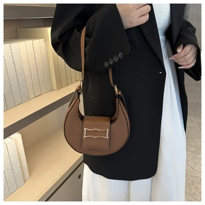 Sac demi-lune en similicuir marron avec boucle dorée porté sur un blazer noir et jupe