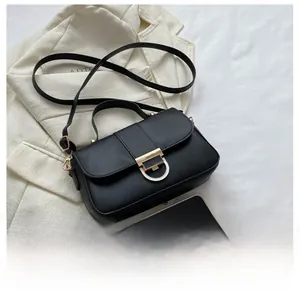 Detail of black crossbody bag with gold D-buckle shown beside phone for size scale