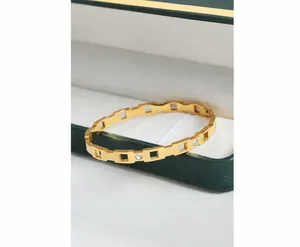 Detalle del brazalete de acero bañado en oro de 18k con geometría hueca y circonitas