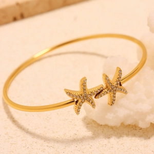 Elegant gold starfish open bangle with sparkling cubic zirconia on coral background