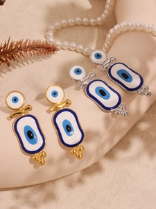 Détail de boucles d'oreilles œil porte-bonheur dorées et argentées en émail sur du sable