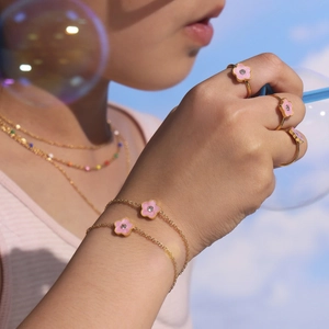 Kinderen sieradenset met roze emaille bloemen en gouden ketting tegen blauwe lucht