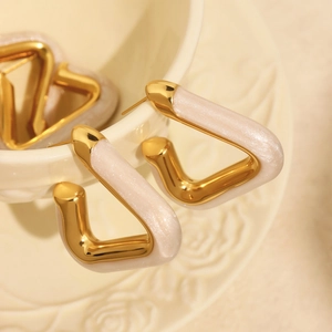Minimalist gold triangular earrings with pearly white inlay on a decorative ceramic cup