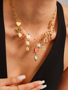 Close-up of layered gold necklace featuring enamel bell, heart, and clover charms on model