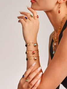 Detail shot of multi-layered gold jewelry set with enamel charms and gemstones