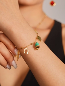 Detail of 18K gold-plated bracelet with horseshoe, chili, and green enamel charms on wrist